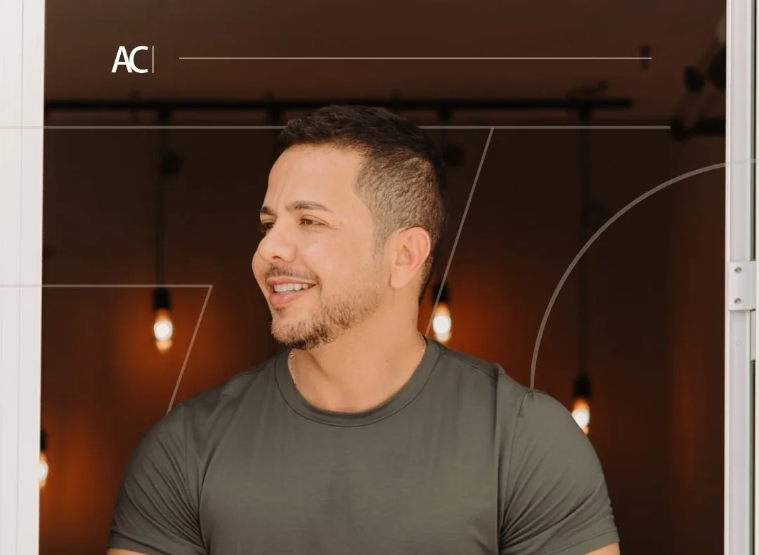 Alexandre Chaves sorrindo, de camiseta verde-oliva, num ambiente com luzes quentes